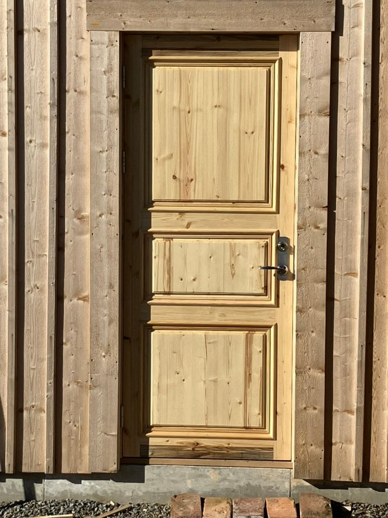 Fyllningsdörr i ljust trä i en fasad av stående träpanel